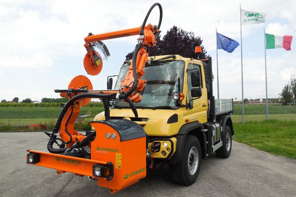 Hymach ROAD-EAGLE MAXI UF straddle-type brush cutter for Unimog, designed for mowing grass around guardrail supports along the road.